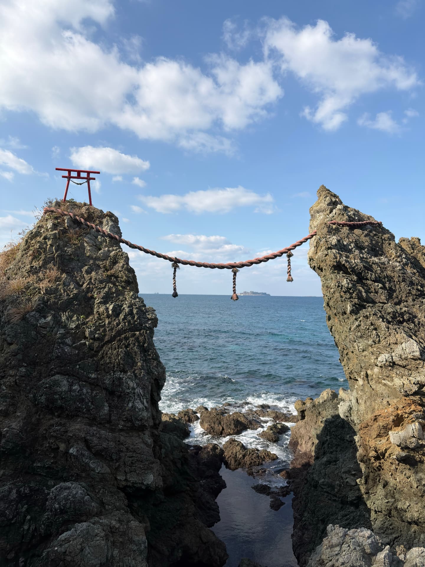 The two Meoto Iwa rocks joined by a shimenawa rope, with a small torii gate, the sea and the sky in Japan.